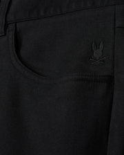 The MENS HAYS TWILL PANT by Psycho Bunny showcases a close-up of black denim fabric, highlighted by a small embroidered logo of a bunny above crossed bones located near the front pocket. This cotton-blend twill design provides ultimate comfort and flexibility with its 4-way stretch, delivering both style and practicality.