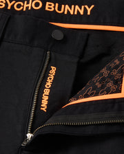 Close-up of the black fabric on the MENS HAYS TWILL PANT - B6P894D200 by Psycho Bunny, featuring orange text "PSYCHO BUNNY" on a zipper and embroidered detail. The lining, made from a cotton-blend twill, showcases a pattern of bunny outlines in orange. Orange piping along the garment's edge adds to its ultimate comfort.