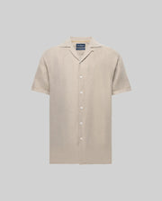 The Psycho Bunny MENS WINDCREST LINEN BLEND SHORT SLEEVE SHIRT (B6Q148C200) is a beige, linen-cotton button-up with short sleeves, notched collar, chest pocket, embroidered logo on the left, and mother-of-pearl buttons against a light gray background.