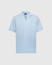 The Psycho Bunny MENS COBAR WOVEN SHIRT (B6Q522F200) is a light blue, short-sleeve linen blend shirt with a camp collar, subtle texture, and tonal logo embroidery on the left chest, shown on a white background.