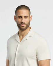 A man with a shaved head and beard wears the Psycho Bunny MENS BRYAN CAMP COLLAR SHORT SLEEVE SHIRT - B6Q581F200 made of performance fabric, against a plain white background.