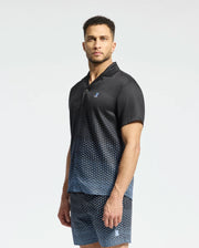 A man stands with a neutral expression against a plain background, wearing a dark Psycho Bunny MENS BENDIGO TENCEL SHIRT - B6Q627F200 featuring an ombre effect and small chest logo, paired with matching shorts.