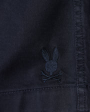 Close-up of a black fabric featuring an embroidered emblem of a stylized bunny skull with crossbones underneath. The stitching is in a subtle shade just a bit lighter than the fabric, creating a sleek and minimalist look—perfect for Psycho Bunny MENS WILLIS STRETCH TENCEL SHORT - B6R239Y1WB.