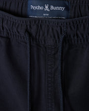 Close-up image of dark blue pants featuring an elastic waistband with a drawstring. The label reads "Psycho Bunny" with a logo of a bunny with crossbones below, indicating the size is medium. These comfortable MENS WILLIS STRETCH TENCEL SHORT - B6R239Y1WB from Psycho Bunny are made in China and designed for ultimate comfort and style.