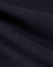 Close-up of a folded piece of dark fabric, showcasing its fine ribbed texture and smooth appearance. The fabric appears dense and slightly shiny, indicating a high-quality material often found in Psycho Bunny's MENS WILLIS STRETCH TENCEL SHORT - B6R239Y1WB. The ridges create subtle waves across the surface.