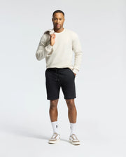 A man in a light long-sleeve shirt and Psycho Bunny's Levanzo Embroidered Micro French Terry Sweatshort, holding a gray jacket over his shoulder. He wears white socks with an embroidered bunny logo and white sneakers, standing against a plain white background.