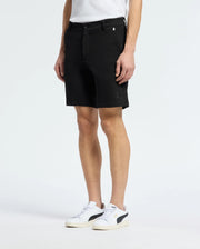A person in MENS SHIRO KNIT HONEYCOMB SHORT by Psycho Bunny, paired with black and white sneakers, stands against a plain white background. The subtle logo near the hem adds flair to these versatile shorts.
