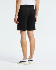 A person stands with their back to the camera, wearing a white shirt and the Psycho Bunny MENS SHIRO KNIT HONEYCOMB SHORT - B6R585F200. White sneakers with black accents complete the look against a plain background, showcasing a stylish transition for any setting.
