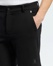 A person wears MENS SHIRO KNIT HONEYCOMB SHORT by Psycho Bunny. Black shorts feature a small embroidered rabbit logo near the pocket and on the leg, showcasing chic simplicity against a plain white background.