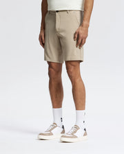 A man models Psycho Bunny’s MENS SHIRO KNIT HONEYCOMB SHORT - B6R585F200 in beige, paired with logo white socks and white sneakers with beige accents, standing against a white background for a stylish, versatile look.