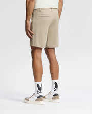 A man, back turned, wears Psycho Bunny MENS SHIRO KNIT HONEYCOMB SHORTS (B6R585F200), white socks with black graphics, white sneakers with tan accents, and a light shirt against a plain white background for a smart-casual look.
