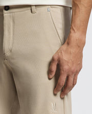 A close-up of a person's right hand by the pocket of Psycho Bunny's MENS SHIRO KNIT HONEYCOMB SHORT—beige, textured piqué with a small white two-leaf logo. The person pairs it with a light-colored top.