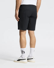 A person wears the MENS 10K STEP SHORT - B6R969F200 by Psycho Bunny and a white T-shirt, matched with white sneakers and logo-printed socks, showing their lower half against a plain background.