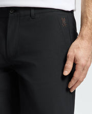 A person wears black MENS 10K STEP SHORT - B6R969F200, featuring athletic breathability and a subtle Psycho Bunny logo by the pocket. Their hand rests by the side, paired with a crisp white shirt.