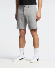 A person wearing Psycho Bunny's light grey MENS 10K STEP SHORT - B6R969F200, paired with a black belt and T-shirt. They're also in white socks and sneakers featuring a black logo, set against a plain, light background.