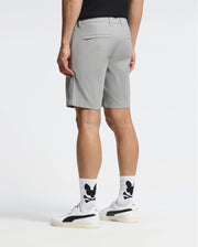The image features a person in Psycho Bunny's MENS 10K STEP SHORT - B6R969F200, with a black T-shirt and white sneakers. They're wearing white socks with black designs, set against a plain white background that emphasizes the athletic breathability, focusing on their lower body from the back.