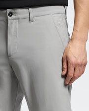 Close-up of a person in Psycho Bunny's MENS 10K STEP SHORT - B6R969F200, featuring breathable light gray fabric and a skull with rabbit ears logo on the upper thigh. They're standing with one hand relaxed at their side, wearing a black top.