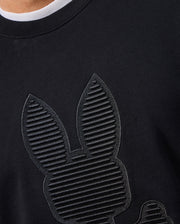 Close-up of a person wearing the MENS KINGSTON SWEATSHIRT by Psycho Bunny. This black cotton jersey shirt features tonal embossing with a textured design showcasing a stylized rabbit head and ears, crafted from horizontal lines to create a remarkable striped effect.