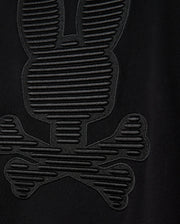 Close-up of the black cotton jersey fabric from the Psycho Bunny MENS KINGSTON SWEATSHIRT (B6S480D200), showcasing a textured design resembling a stylized bunny skull and crossbones. The pattern features tonal embossing with horizontal lines that add detail, creating a 3D-embroidery effect on the sweatshirt.
