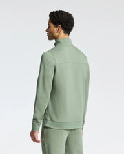 Dressed in a Psycho Bunny men's desert 1/4 mock zip (B6S488F200), featuring an embroidered logo, a person with short curly hair stands against a plain white background in a light green cotton tracksuit.