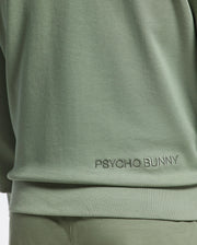 Close-up of a person wearing a Psycho Bunny MELBOURNE Crewneck in light green with lower back embroidery, crafted from a smooth Modal blend. Matching green pants are partially visible below.