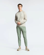 Against a plain white background, a person wears a Psycho Bunny MENS ARCHIE MELANGE COLOR BLOCK SWEATSHIRT alongside pale green cargo pants and white and beige sneakers. Their hands rest in front, creating an effortlessly stylish look.