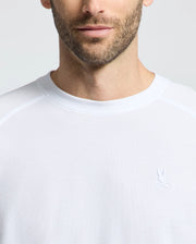 A man wears the Psycho Bunny MENS TAYLOR PIQUE LONG SLEEVE TEE, made from soft Pima cotton with a small embroidered bunny logo on the chest. The image showcases the elegant piqué knit texture against a plain, light-colored background.