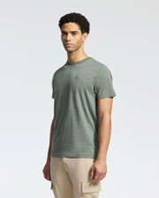 A man showcases the Psycho Bunny MENS CLASSIC CREW NECK TEE, made from Pima cotton in green with an embroidered logo, paired with beige cargo pants on a white background, delivering a relaxed regular fit.