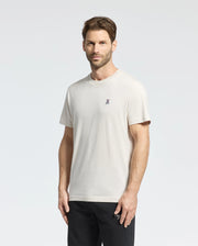 A man with short brown hair wears a Psycho Bunny Men's Classic Crew Neck Tee in premium jersey with a small embroidered chest logo, paired with black pants. He stands against a plain white background, looking at the camera neutrally.