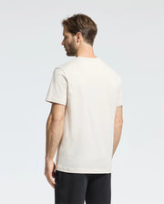 A man with short brown hair is seen from behind, wearing a Psycho Bunny MENS CLASSIC CREW NECK TEE - B6U014B200 made of premium jersey. His plain white T-shirt contrasts subtly against the light-colored background alongside his black pants.