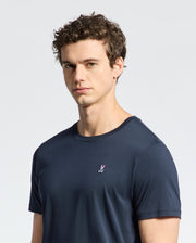 A young man with short curly hair wears the Psycho Bunny MENS CLASSIC CREW NECK TEE - B6U014CRPC in navy blue, featuring a small embroidered bunny logo on the chest, standing against a plain light background.