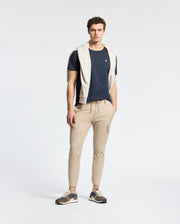 A man faces forward, wearing a Psycho Bunny MENS CLASSIC CREW NECK TEE - B6U014CRPC in navy (100% Pima cotton), paired with light beige joggers, multicolored sneakers, and a light gray sweater over his shoulders against a plain background.