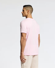 A man with short dark hair is wearing the Psycho Bunny MENS CLASSIC CREW NECK TEE (B6U014CRPC) in light pink and beige shorts, standing against a plain background, looking to the side.