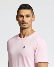 A man with short black hair and a trimmed beard wears the Psycho Bunny MENS CLASSIC CREW NECK TEE - B6U014CRPC in light pink, made from soft pima cotton with a small embroidered logo on the chest. He stands against a plain, light-toned background.