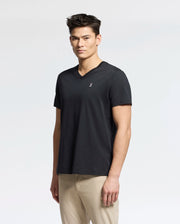 A person with short dark hair wearing a Psycho Bunny Men's Classic V Neck Tee (B6U100ARPC) in black and beige pants stands against a plain white background.