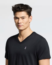 A person with short dark hair is wearing a Psycho Bunny MENS CLASSIC V NECK TEE, B6U100ARPC, featuring a small embroidered emblem on the chest. They are standing against a plain background and looking directly at the camera.