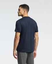 The man with short curly hair stands facing away, wearing a Psycho Bunny MENS CLASSIC V NECK TEE - B6U100ARPC in navy blue and gray pants against a plain light background.