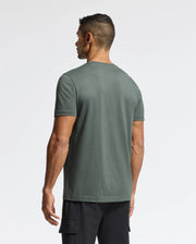A man is seen from behind, wearing a dark green Psycho Bunny MENS PIERCE EMBROIDERED GRAPHIC TEE - B6U115E200 made of soft Pima cotton paired with black cargo shorts, set against a plain white background.