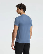 A man with curly hair is seen from behind, wearing a Psycho Bunny MENS MONARC FRONT BUNNY GRAPHIC TEE - B6U211E200 made of 100% Pima cotton and black pants, standing against a plain white backdrop.