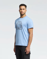 A person with short curly hair wears a light blue Men's Melbourne Graphic Tee (B6U410F200) by Psycho Bunny featuring a stylized rabbit. They stand against a plain background, looking directly at the camera, blending style and sustainability.