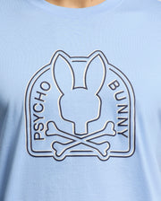 Close-up of the light blue MENS MELBOURNE GRAPHIC TEE by Psycho Bunny, made from eco-friendly Peruvian Pima cotton. It showcases a stylized rabbit head above crossbones with "Psycho Bunny" around the logo.