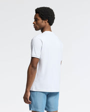 A person wearing the Psycho Bunny MENS BRYCE PERFORMANCE TEE - B6U490F200, a slim fit white T-shirt, and light blue Modal-Pima cotton blend shorts looks to their left against a plain white background.