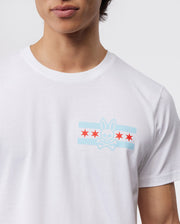 A person wearing a Psycho Bunny MENS CHICAGO CITY TEE - B6U551W1PC in Pima cotton, with a light blue and red bunny logo above crossed bones on the chest and three red stars below, set against a plain gray background.