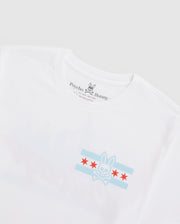 The Psycho Bunny MENS CHICAGO CITY TEE - B6U551W1PC is a white Pima cotton tee showcasing light blue and red flag-like stars. Featuring the classic logo and distinct branding inside the neckline, it blends comfort with style effortlessly.