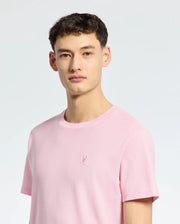 A young man with short brown hair wears the Psycho Bunny MENS TAYLOR PIQUE TEE (B6U579F200) in light pink piqué, featuring an embroidered chest Bunny, standing against a plain light background.