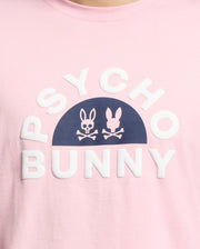 The MENS GOLDIE GRAPHIC TEE - B6U606F200 by Psycho Bunny is made from Peruvian Pima cotton. It features a pink color with navy bunny skull graphics above bold white "PSYCHO BUNNY" lettering.