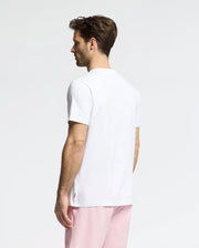 A man, with short brown hair, stands against a plain white background wearing the Psycho Bunny MENS GOLDIE GRAPHIC TEE (B6U606F200), a playful bunny on his white T-shirt, and pink shorts.