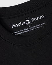 Close-up of the neckline and inner clothing label of a black MENS DUKE OVERSIZED TEE - B6U742D200 from Psycho Bunny. The label shows the brand name and logo, detailing "100% heavyweight Pima cotton," "Made in Peru," and featuring an embroidered chest bunny on this relaxed fit design.