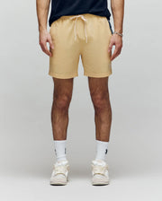 A person wearing Psycho Bunny MENS SAMOS HYDROCHROMIC PRINTED SWIM TRUNK (B6W453F200) in beige, paired with white crew socks and sneakers, stands against a plain light background. Only their lower torso and legs are visible.
