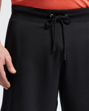 A person is shown from the waist down wearing Psycho Bunny MENS BIG AND TALL LEVANZO EMBROIDERED MICRO FRENCH TERRY SWEATSHORT (B9R578F200), with focus on the black shorts' drawstring tie. The image also shows part of one hand and a red shirt.